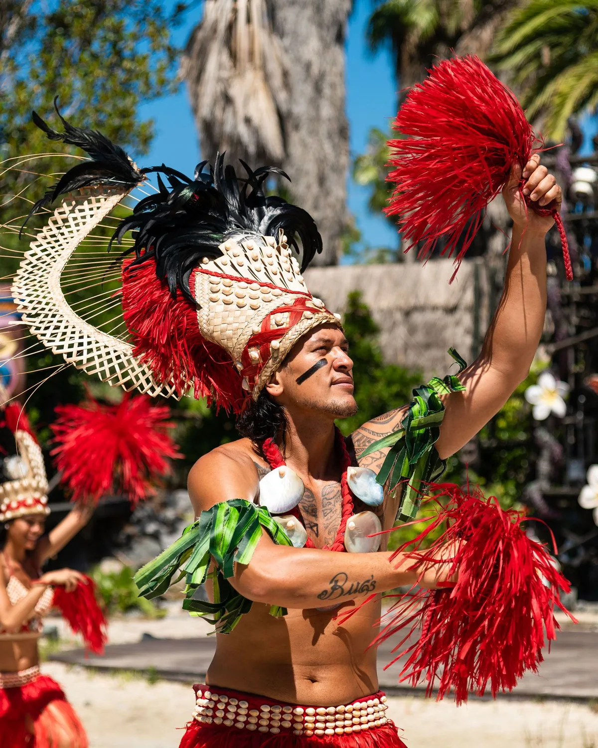 A Polynesian dancer in a feathered headdress mid-performance, arm raised (representative photograph of a Pacific-islands dance, not Chief's Luau itself)