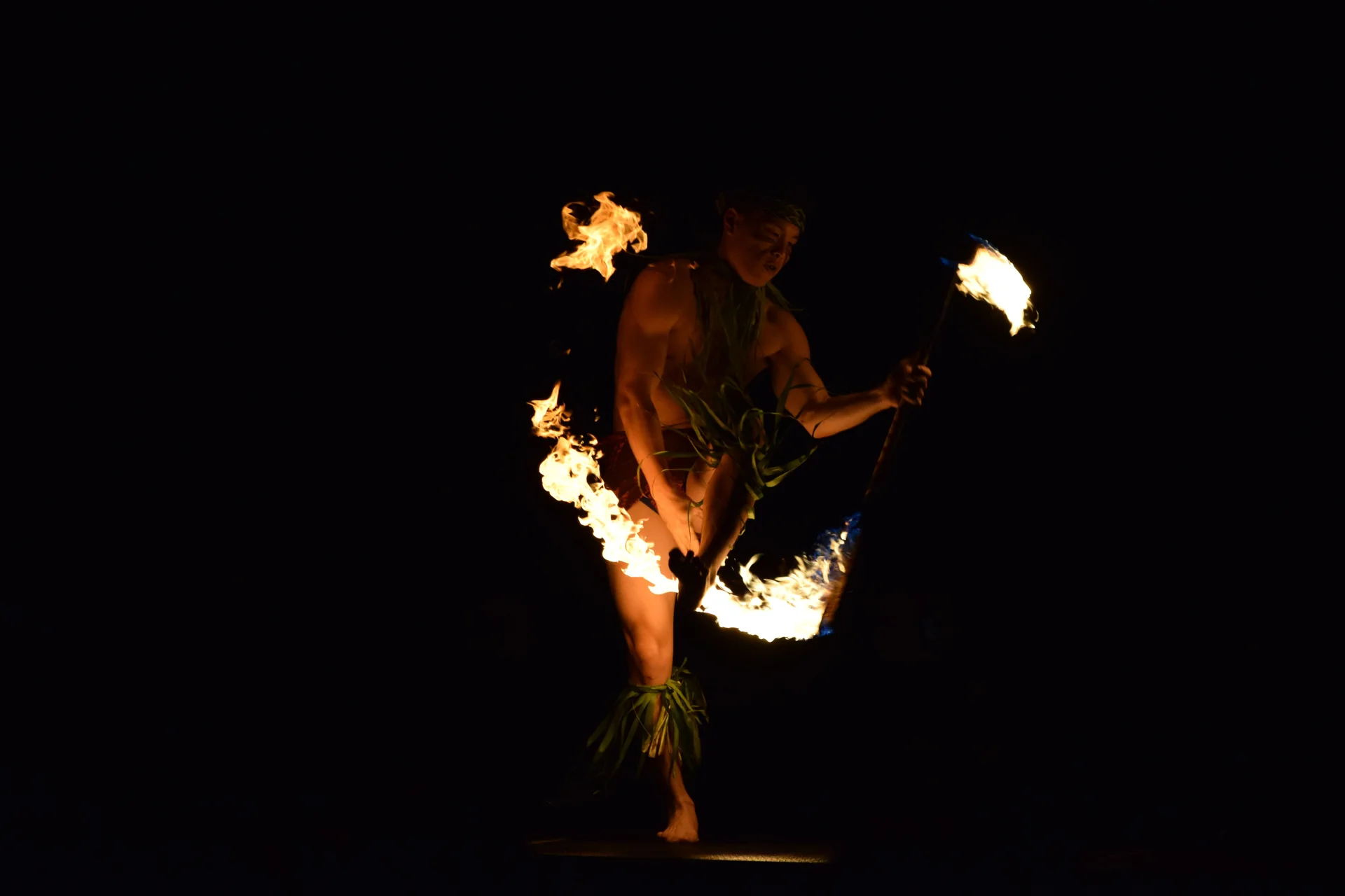 A Polynesian fire-knife dancer mid-performance against a black night stage, flames arcing from a double-bladed torch (representative photograph of a fire-knife performance, not Chief's Luau itself)